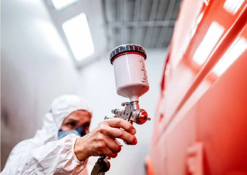 Pintor aplicando con pistola sobre una carrocería roja