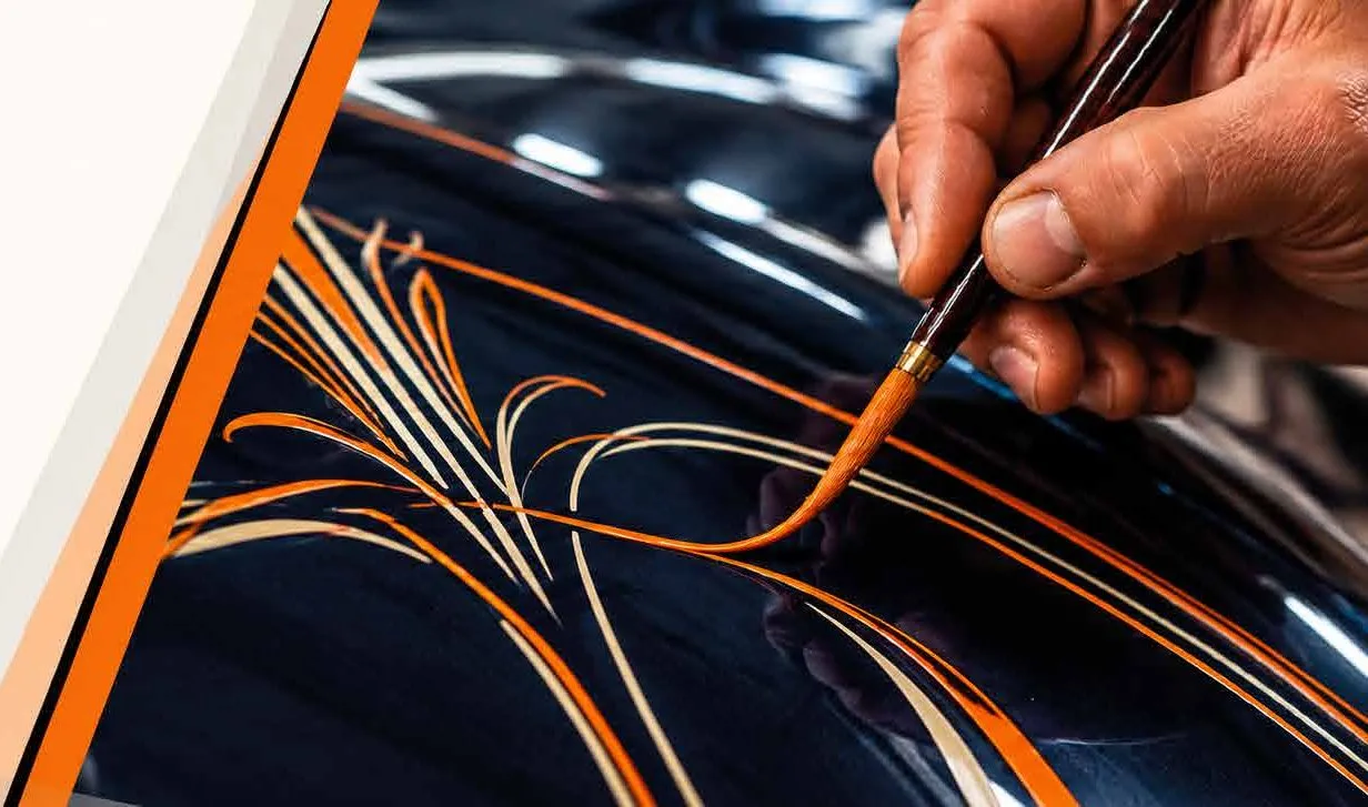 Pintor trazando filetes naranjas con pincel de pinstriping sobre una carrocería negra